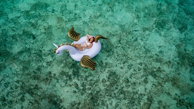 女人穿着白色比基尼躺在白色和棕色的独角兽充气浮
